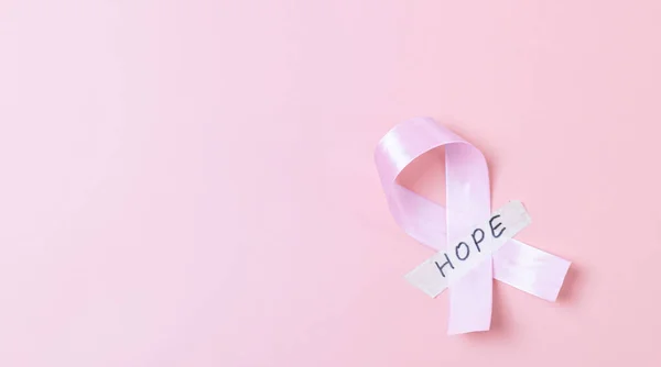 One wide satin pink ribbon with sticky tape with the word: hope lies on the right on a pink background with copy space on the left, flat lay close-up. Concept for world cancer day, breast cancer.