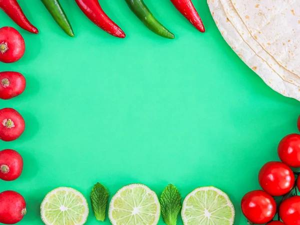 Vegetable frame made of radish, lime, mint, chilli pepper and pita bread with copy space in the center on a green background, flat closeup. Cinco de Mayo concept, minimalism, blanks.