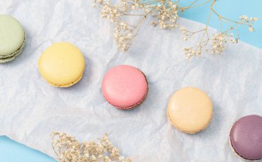 Beş badem kurabiyesi soluk pembe bir kağıt peçetenin üzerinde soluk mavi arka planda çapraz olarak kurumuş çiçekler serpiştirilir. Tatlı tatlı konsepti..