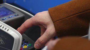 Kahverengi paltolu genç beyaz bir adamın eli dükkandaki düğmelere dokunarak ödeme yapıyor. Yakın plan. Alışverişe çıkan adam kavramı..
