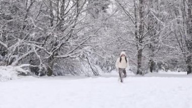 Beyaz ceketli, kahverengi pantolonlu güzel, beyaz tenli esmer kadın kış ormanlarında tökezliyor ve konuşuyor. Kış yürüyüşü kavramı.