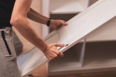 Genç, beyaz bir adam, yatak odasında dikilirken gardıropta yan kapıyı tutuyor. Mobilya montaj konsepti.