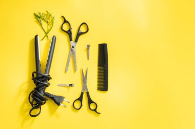 Makas, tarak ve yeşil çiçekli mini bir saç düzleştirici sarı arka planda duruyor, sağ tarafta fotokopi alanı var, düz yakın plan. Kuaför konsepti.