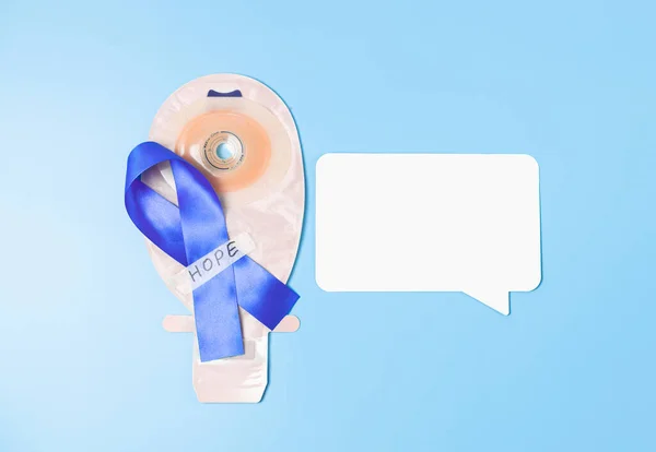 One blue ribbon with sticky tape saying: hope, colostomy bag and and empty white callout lie in the center on a blue background with copy space,flat lay closeup.Concept for world cancer day,abdominal