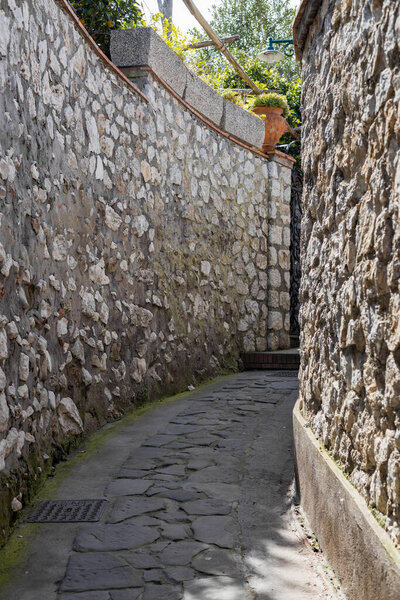 Beautiful side view of a narrow stone street with a high fence and a turn to the right on a summer sunny day on the island of Capri, Italy, close-up side view.