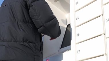 Kot pantolonlu ve ceketli bir genç parmağını terminalin ekranına koyar ve kutudan bir paket almak için akıllı telefondan barkodu tarar.