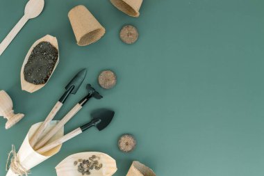 İki spatuladan oluşan üç bahçe aleti, bir tahta konide bir tırmık, çamurlu el işi bardaklar ve botlar solda yeşil bir arka planda, fotokopi alanı olan yarım daire şeklinde yatıyorlar, yakın plan düz. Bahçe işleri, tohum ekme kavramı.