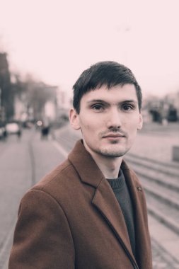 Kahverengi paltolu, yakışıklı, esmer bir adamın portresi şehirde dolanıp kameraya yakından bakıyor. Erkek yaşam tarzı konsepti..