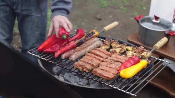 年轻的高加索人把红辣椒放在烤架上 烤上有切碎的肉片和香肠 在房子后院里的烤架上用煤煎 慢镜头中的特写侧视 — 图库视频影像