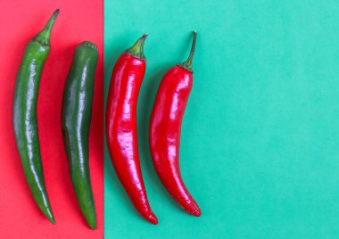 Dört kırmızı biber kırmızı-yeşil arka planda sol sırada yatar, sağ tarafta küçük bir kopya alanı, düz yakın plan. Cinco de Mayo konsepti, minimalizm, boşluk.