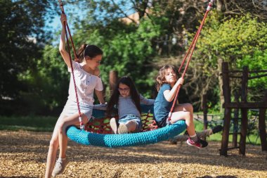 Üç güzel beyaz kız kardeşin portresi oyun parkındaki salıncakta salıncakta yuvarlak bir halatla, yakın çekimde. Park ve REC kavramı, mutlu çocukluk, çocuk pikniği, tatiller, çocuk eğlencesi, açık hava eğlencesi