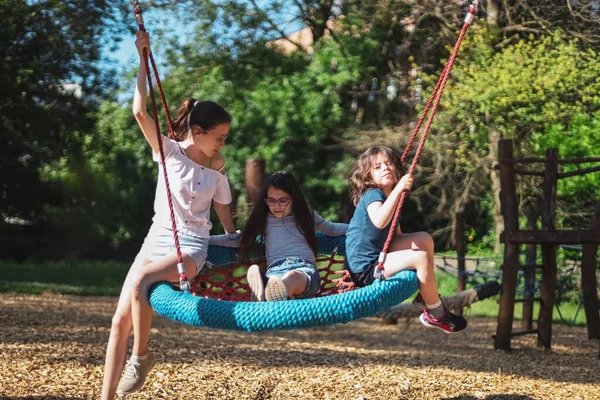 stock image Portrait of three beautiful caucasian girls sisters ride together on a round rope swing in the park at the playground, close-up side view. The concept of PARKS and REC, happy childhood, children's picnic, holidays, children's recreation, outdoor recr