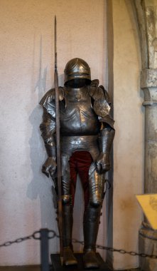 One set of knightly armor with a helmet and a sword stand near the wall in the medieval castle of the city of Luxembourg, side view, close-up with a blurred background. Medieval lifestyle concept.