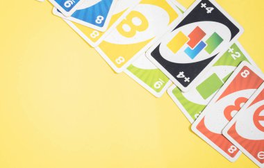 Eski, kirli, renkli uno oyun kartları sarı zemin üzerinde köşegen olarak yatar. Fotokopi alanı solda, düz yakın plan yatar. Masa oyunları kavramı.