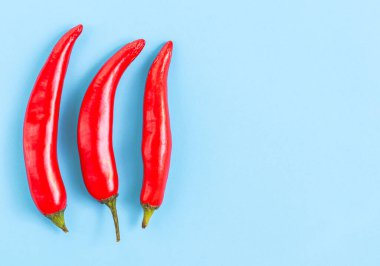 Üç kırmızı kırmızı biber solda açık mavi bir zemin üzerinde uzanıyor. Sağ tarafta fotokopi alanı var. Yakın plan düz. Cinco de mayonez konsepti, minimalizm, boşluk.