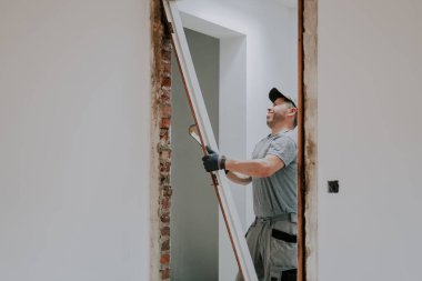 Üniformalı ve gri tekstil eldivenli genç beyaz bir adam gözlerini tozdan kapıyor levye kullanarak bir tahtayı söküyor, seçici bir odak noktasıyla yakın plan yan görüş. İnşaat işi kavramı.