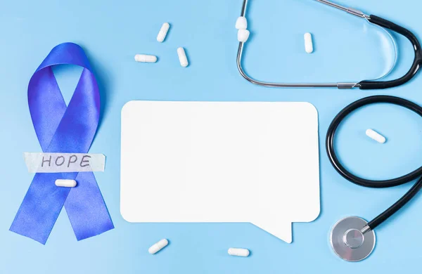 One blue ribbon with sticky tape with the word: hope, stethoscope,empty callout and scattered pills on a blue background with copy space,flat lay closeup.Concept for world cancer day,abdominal diseases.