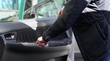 Genç bir Kafkasyalı, güneşli bir bahar gününde, açık bir araba yıkama yerinde, yolcu koltuğunun iç kapısını süpürüyor..