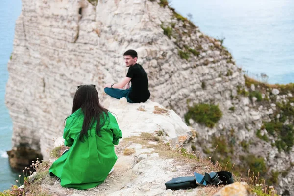 Arkadan gelen beyaz tenli genç bir çift dağlarda oturur ve Etretat, Normandiya, Fransa 'da kuzey denizi yakınlarındaki bir akıllı telefondan fotoğraf çeker..