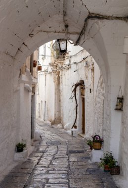 İtalya 'nın Ostuni şehrinde kemer ve saksı çiçekli, dar, güzel bir cadde manzarası var..