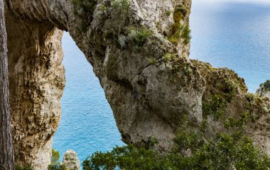 Capri İtalya adasındaki Tirania Denizi 'nin arka planına karşı kayadaki doğal kemerin güzel manzarası..