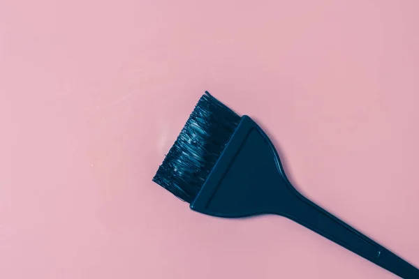 One black hair coloring brush with white cream paint on a pink background with small copy space, flat lay close up. The concept of cosmetics, strokes, isolation.