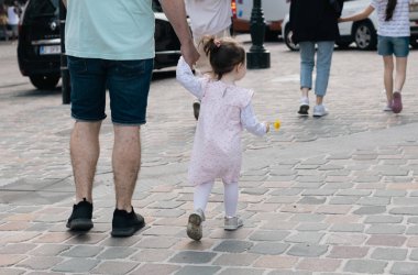 Genç, beyaz bir baba, elinde sarı bir karahindiba ile küçük kızını tutuyor ve bir bahar günü şehir caddesinde yürüyordu. Yakın çekim manzarası. İnsanları arkadan yürütme kavramı..
