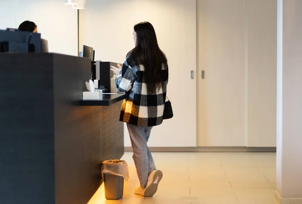 stock image One young caucasian brunette woman with flowing hair in a plaid shirt is standing behind a reception desk in a dentistry talking to an administrator, side view close-up.