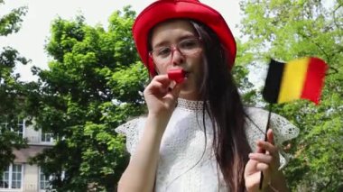 Belçika bayrağı şapkalı güzel beyaz bir kız parktaki çimenlikte dikilmiş Belçika Bağımsızlık Günü 'nü yakından izlerken bir tomar tomar sallıyor. Belçika Günü konsepti.