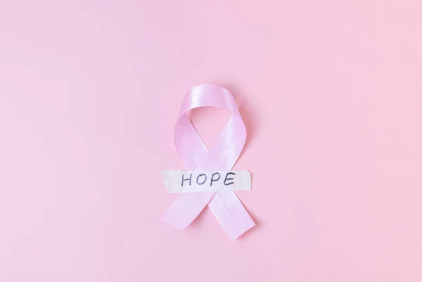 One wide satin pink ribbon with sticky tape with the word: hope lie in the center on a pink background with copy space on the sides, flat lay close-up. Concept for world cancer day, breast cancer.