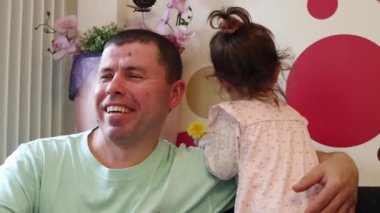 Genç yakışıklı beyaz bir adam bir kafede oturuyor ve küçük kızıyla oynaşırken gülümsüyor..