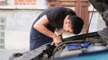 Kafkasyalı bir genç tornavidayla vidaları söküyor ön kaputun sağ ön farında yanmış bir ampul, yakın plan yan görüş. Araba ampulünü değiştirme kavramı..