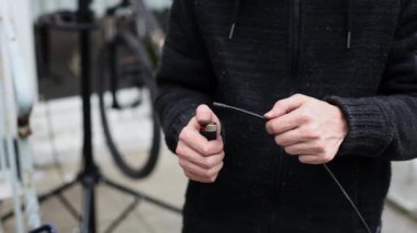 Beyaz bir genç, bir bisiklet için fren kablolarının üzerinde çakmak tutuşturuyor, evin arka bahçesinde dikiliyor, yakından bakıyor. Bisiklet tamir konsepti.