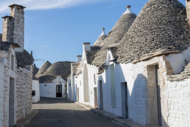 Çiçeklerin döndüğü dar bir caddenin güzel manzarası ve güneşli bir günde Alberobello şehrindeki ünlü Trulli evleri, puglia, italyan manzara.