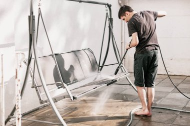 Siyah elbiseli, esmer, beyaz bir adamın portresi. Çıplak ayakla evinin arka bahçesinde salıncağını yıkıyor..