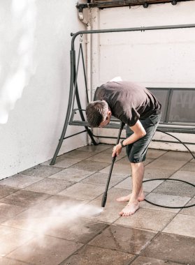 Siyah elbiseli esmer beyaz bir adamın portresi eğimli bir pozisyonda yalın ayak evinin arka bahçesinde bahçe fayanslarını yıkıyor basınçlı su püskürtüsüyle, yan tarafından yakın çekim görüntüsüyle..