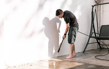 Siyah elbiseli esmer bir gencin portresi yalın ayak bahçe fayanslarını yıkamak için eğilmiş bir şekilde evinin arka bahçesindeki beyaz bir duvarın yanında bir kerpetenle, sol tarafında fotokopi alanı olan yakın çekim kenarı manzaralı..
