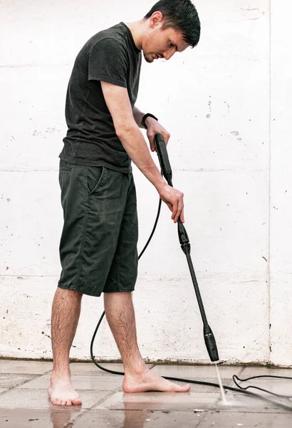 Siyah elbiseli, esmer, beyaz bir adamın portresi evinin arka bahçesinde döşemeyi yıkıyor. Kretcher ile yakın çekim manzarası var..