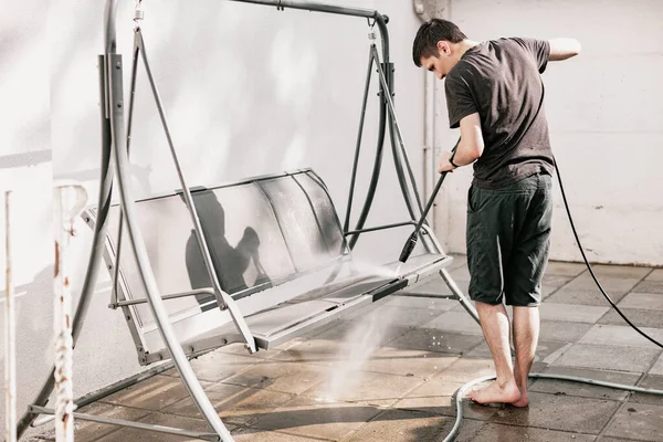 Siyah elbiseli, esmer, beyaz bir adamın portresi. Çıplak ayakla evinin arka bahçesinde salıncağını yıkıyor..