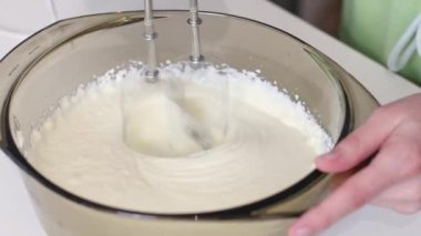 Genç, beyaz, tanınmayan bir kız, pastaya krema yapmak için cam bir kasede peynir kütlelerini yeniyor. Mutfakta beyaz bir masada dikiliyor, yan gözle bakılıyor. Pasta yapmak için adım adım talimatlar alın..
