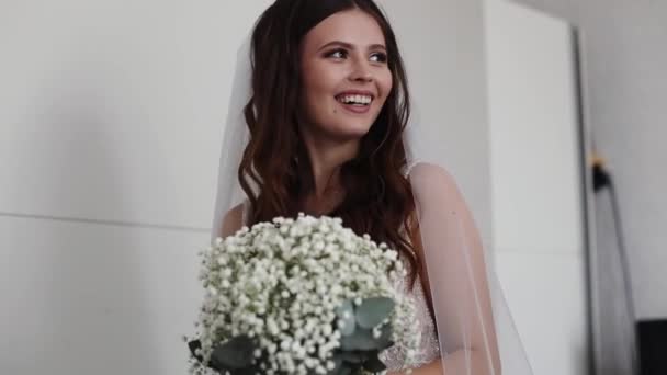 美しい若い白人ブルネットの花嫁は 彼女の顔に幸せな笑顔の花束が部屋に立っているグルメとの会議を待っています クローズアップサイドビュー — ストック動画