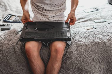Genç, beyaz, tanınmayan bir adam tamir sonrası yedek parçaları laptopa bağlıyor, bir odada bir yatağın üzerinde oturuyor, yakın çekim yan görüntüsü. Adım adım dizüstü bilgisayar tamiri ve termal yapıştırıcı değişimi kavramı.
