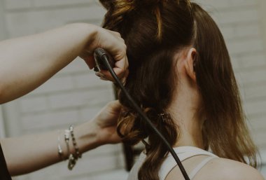 Kafkasyalı genç bir kızın portresi, bir kuaförün dükkanında arkada oturuyor, usta saçını düz ütüyle kıvırıyor, yakın çekim manzarası var..