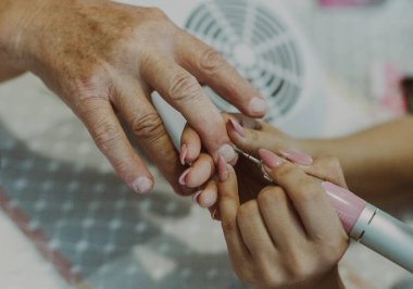 Bir manikürcü, yaşlı bir kadının elinde kesiciyle tırnak etlerini temizler. Manikür yapar, yakından bakar..