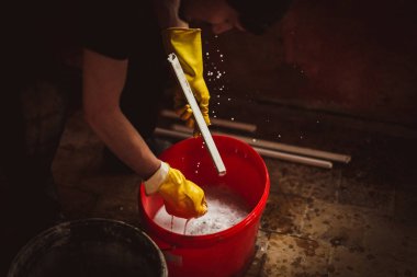 Kafasında şapkası ve sarı lastik eldivenleri olan beyaz, genç bir adam sabunlu bir kovada pencere çerçevelerini yıkar, süngerle sıkar, bir odada eğilip...