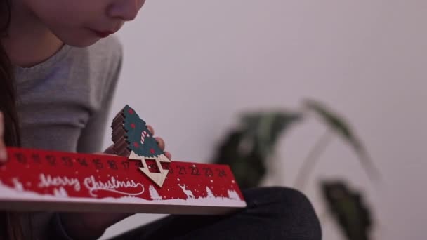 小女孩高加索手将木圣诞树移动到红色尺子日历上的第19号和第20号 坐在床上 慢吞吞地侧视特写 — 图库视频影像