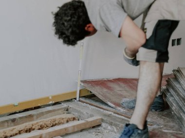 Üniformalı ve eldivenli genç bir adam, bir açıda duran, odaya şömine koymak için bir inşaat cetvelli bir duvar ölçer, yakın görüş. Ev yenileme, inşaat işi kavramı.