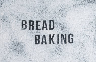 Dağınık un üzerine yazılmış yazı: Ekmek ortada, siyah taş bir masanın üzerinde, düz bir şekilde yakın plan uzanıyor. Ekmek pişirme konsepti.