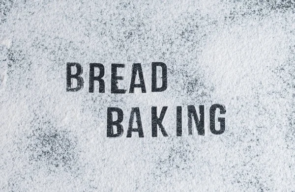 Dağınık un üzerine yazılmış yazı: Ekmek ortada, siyah taş bir masanın üzerinde, düz bir şekilde yakın plan uzanıyor. Ekmek pişirme konsepti.