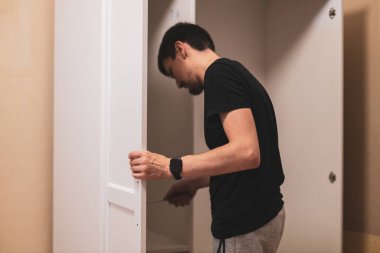 Genç beyaz tenli esmer adam, elleri gardırobun yan kapısında yatak odasında dikilirken vidayı vidalıyor. Mobilya montaj konsepti.